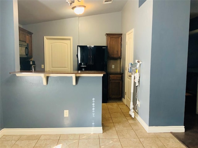 kitchen featuring black refrigerator with ice dispenser, kitchen peninsula, lofted ceiling, a kitchen bar, and light tile patterned floors