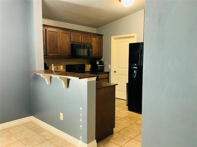 kitchen featuring a kitchen breakfast bar, kitchen peninsula, vaulted ceiling, light tile patterned floors, and black appliances