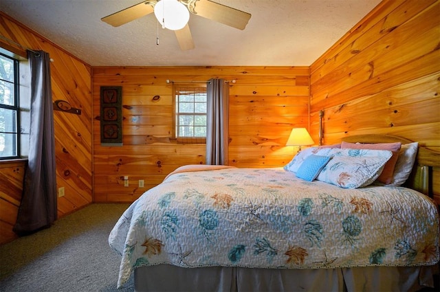 carpeted bedroom featuring multiple windows, wooden walls, and ceiling fan