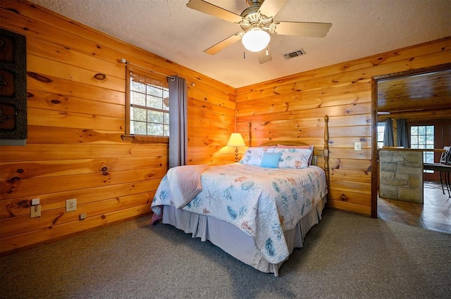 carpeted bedroom with wooden walls, ceiling fan, and a textured ceiling