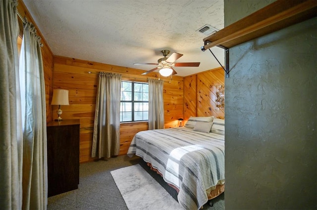 carpeted bedroom with a textured ceiling, ceiling fan, and wood walls