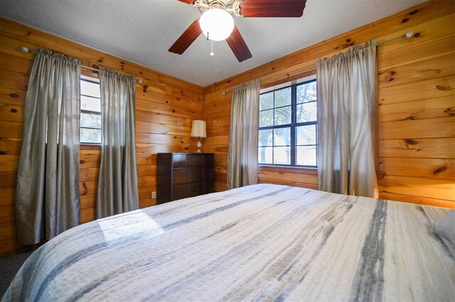 bedroom with a textured ceiling, ceiling fan, and wooden walls