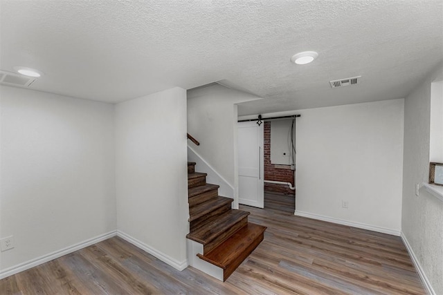 staircase featuring wood-type flooring, a barn door, and a textured ceiling