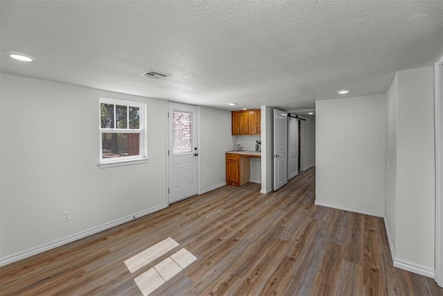 unfurnished living room with a textured ceiling, a barn door, and light hardwood / wood-style floors