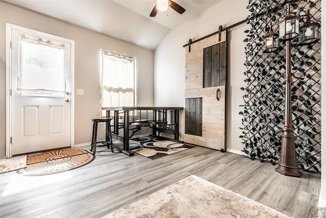 foyer entrance featuring a barn door, ceiling fan, lofted ceiling, and light wood-type flooring