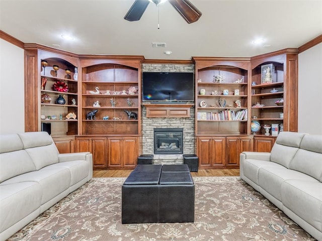 living room with a stone fireplace, built in features, ornamental molding, and light wood-type flooring