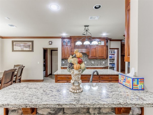 kitchen featuring tasteful backsplash, crown molding, hanging light fixtures, and light stone counters