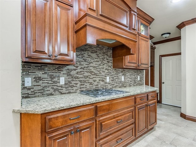 kitchen with light stone countertops, backsplash, ornamental molding, custom exhaust hood, and stainless steel gas cooktop