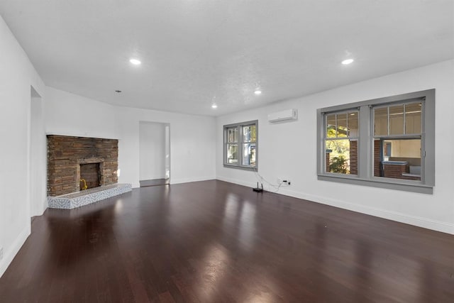 unfurnished living room featuring a fireplace, hardwood / wood-style flooring, and a wall mounted air conditioner