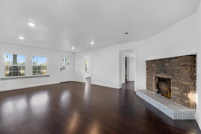 unfurnished living room with a textured ceiling, dark wood-type flooring, and a stone fireplace