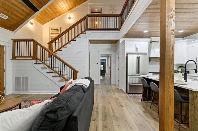 living room with wood walls, wooden ceiling, sink, vaulted ceiling, and light wood-type flooring