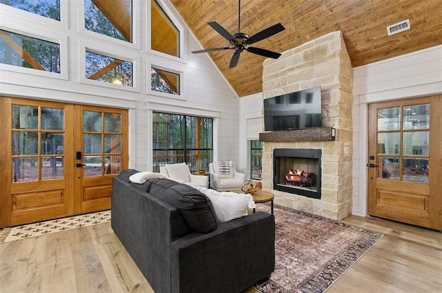 living room featuring a stone fireplace, plenty of natural light, high vaulted ceiling, and light wood-type flooring