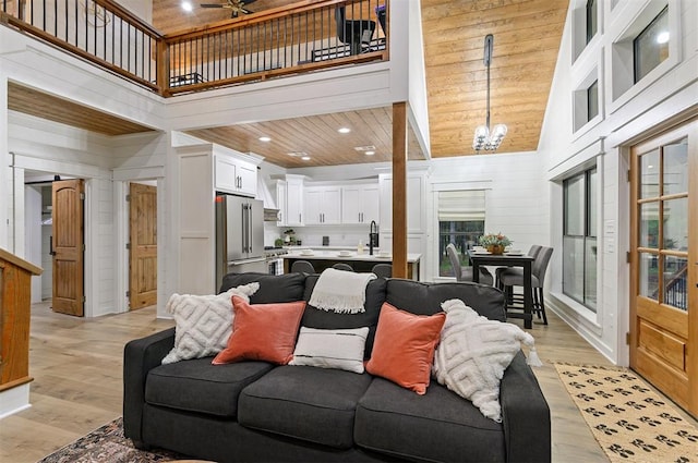 living room featuring sink, wooden ceiling, light hardwood / wood-style flooring, high vaulted ceiling, and ceiling fan with notable chandelier