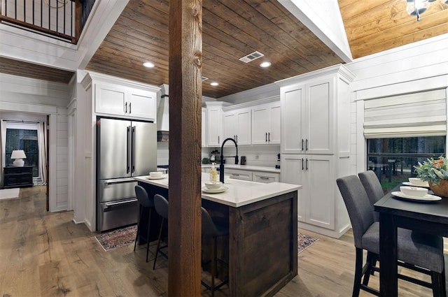 kitchen with a kitchen bar, white cabinetry, an island with sink, and stainless steel refrigerator