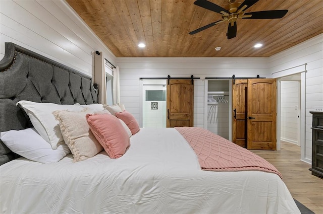 bedroom featuring ceiling fan, wooden ceiling, a barn door, wood walls, and light hardwood / wood-style floors