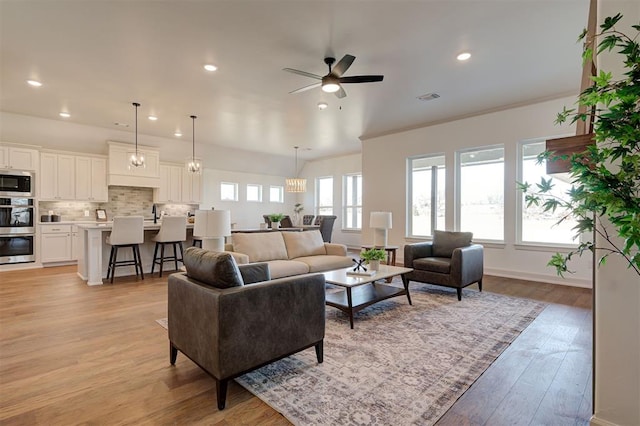 living area with ornamental molding, light wood-type flooring, visible vents, and recessed lighting