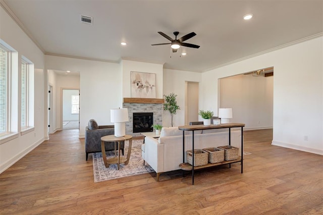 living room featuring light wood-type flooring, visible vents, ornamental molding, and a glass covered fireplace