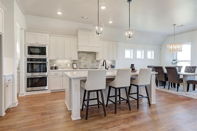 kitchen featuring a breakfast bar, light wood finished floors, stainless steel appliances, decorative backsplash, and an island with sink