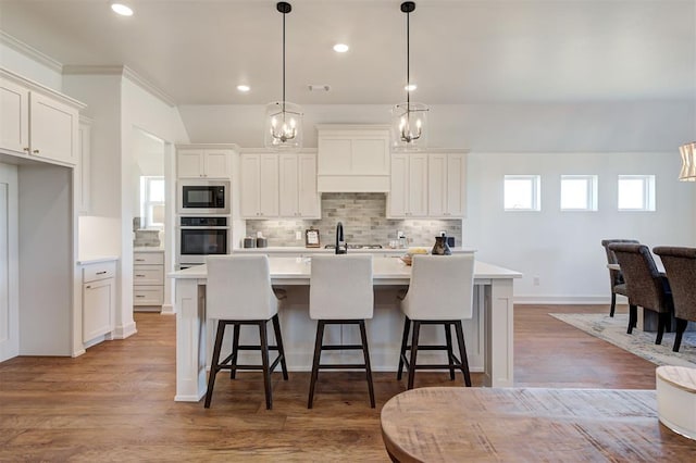 kitchen featuring stainless steel oven, light countertops, backsplash, built in microwave, and a center island with sink