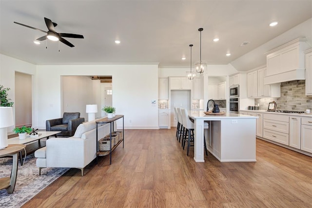 kitchen featuring stainless steel appliances, light countertops, decorative backsplash, light wood-style floors, and open floor plan