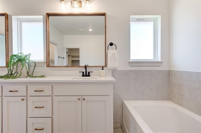 bathroom featuring vanity, a bath, and tile walls