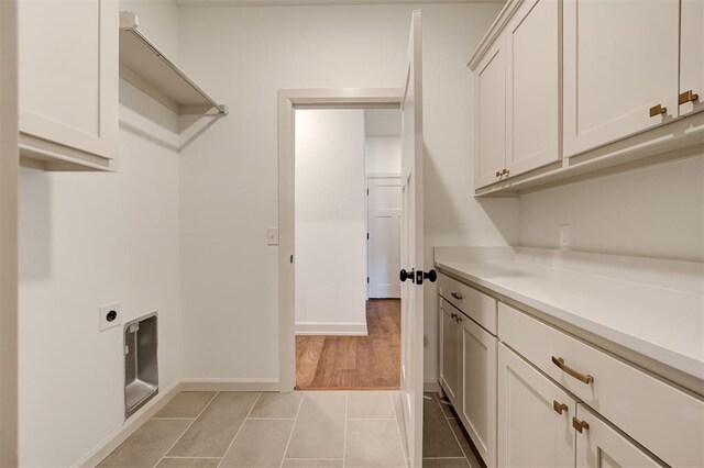 clothes washing area with baseboards, light tile patterned flooring, cabinet space, and electric dryer hookup