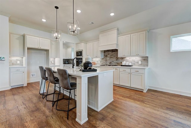 14500 Rushing Ln, Edmond, OK 73025 - kitchen featuring appliances with stainless steel finishes, decorative backsplash, premium range hood, light countertops, and an island with sink