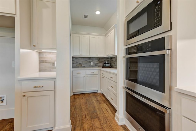 14500 Rushing Ln, Edmond, OK 73025 - kitchen with built in microwave, wood finished floors, light countertops, tasteful backsplash, and stainless steel double oven
