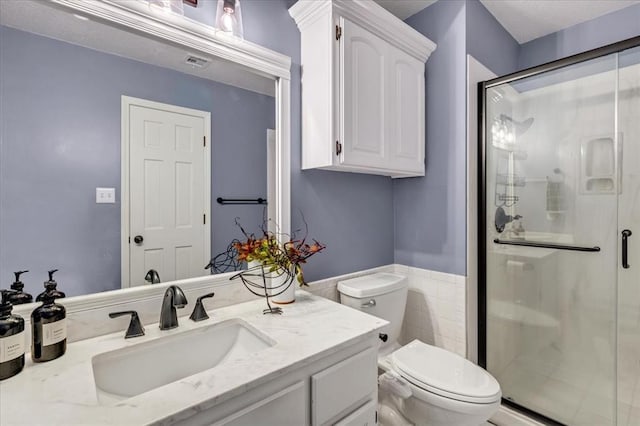 bathroom featuring toilet, tile walls, vanity, and a shower with shower door