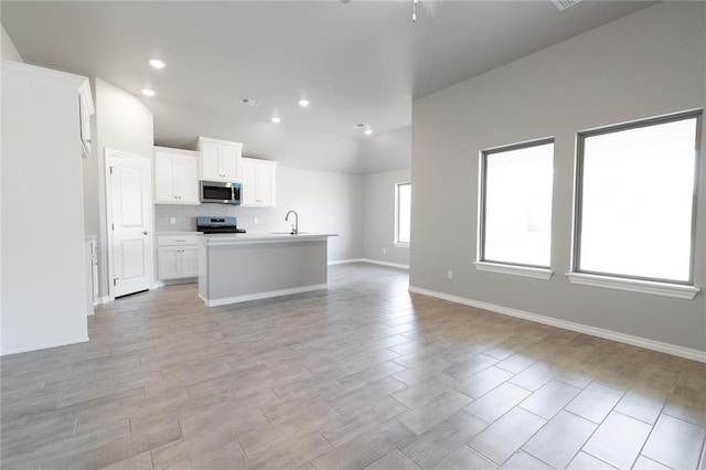 kitchen with an island with sink, open floor plan, white cabinetry, lofted ceiling, and appliances with stainless steel finishes