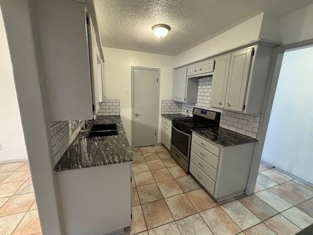 kitchen with tasteful backsplash, stainless steel gas range oven, a textured ceiling, sink, and dark stone countertops