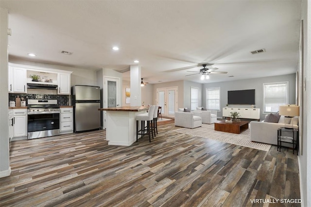 kitchen with stainless steel appliances, ceiling fan, dark wood-type flooring, white cabinetry, and a breakfast bar area