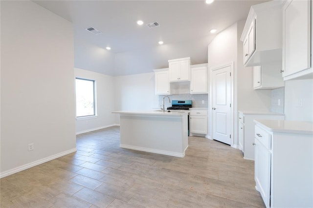 kitchen with tasteful backsplash, visible vents, and an island with sink