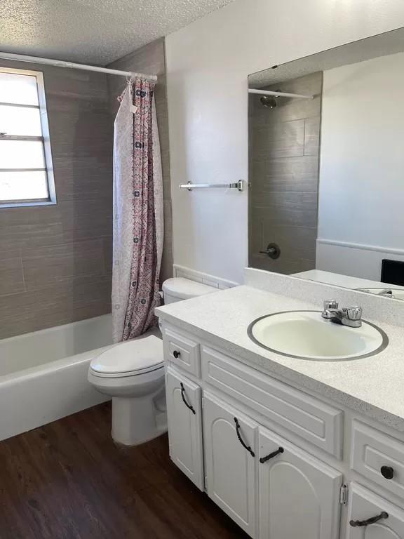 full bathroom featuring vanity, toilet, a textured ceiling, wood-type flooring, and shower / tub combo