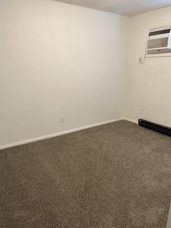 carpeted spare room featuring a textured ceiling and an AC wall unit