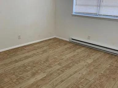 spare room with wood-type flooring and a baseboard heating unit