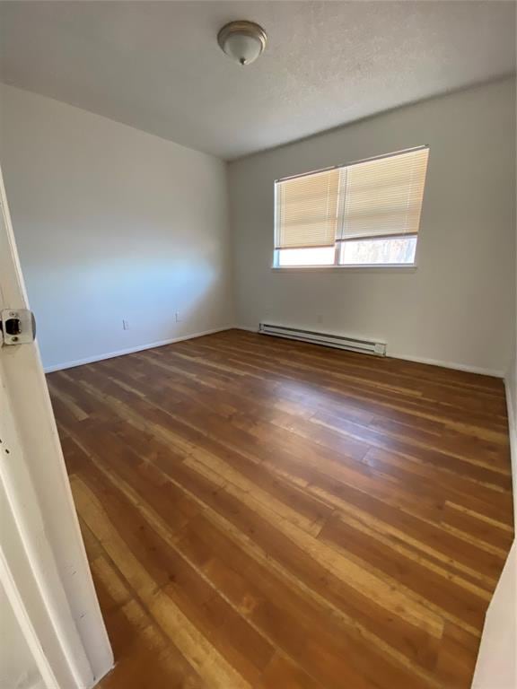 unfurnished room featuring dark hardwood / wood-style flooring and a baseboard heating unit