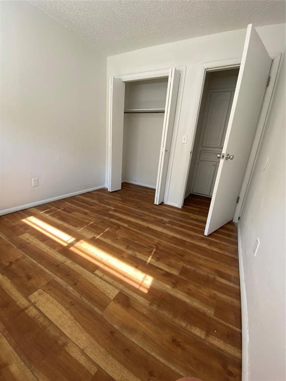 unfurnished bedroom with a textured ceiling, dark hardwood / wood-style floors, and a closet