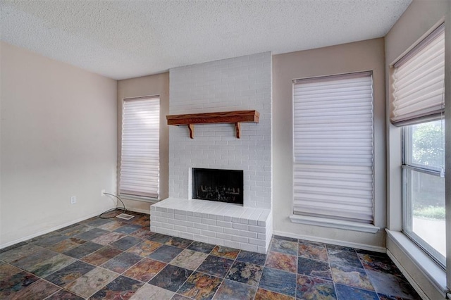 unfurnished living room with plenty of natural light, a textured ceiling, and a brick fireplace