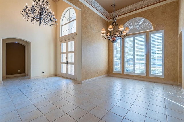 tiled empty room with a wealth of natural light, arched walkways, crown molding, and an inviting chandelier