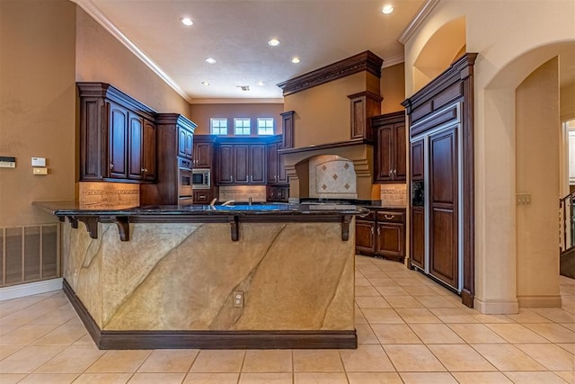 kitchen with dark countertops, visible vents, built in appliances, a peninsula, and a kitchen breakfast bar