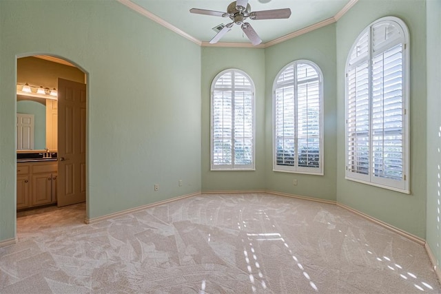 spare room with a ceiling fan, arched walkways, crown molding, and light colored carpet