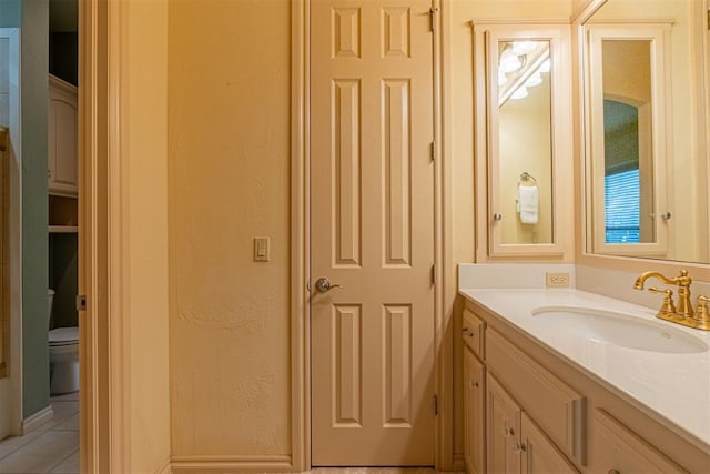 bathroom featuring toilet, a textured wall, tile patterned flooring, and vanity