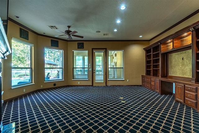 interior space with a ceiling fan, visible vents, built in desk, carpet, and crown molding