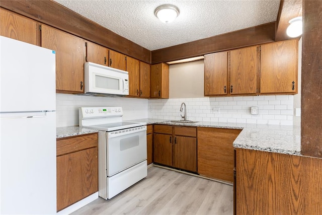 kitchen with a textured ceiling, white appliances, light hardwood / wood-style flooring, and backsplash