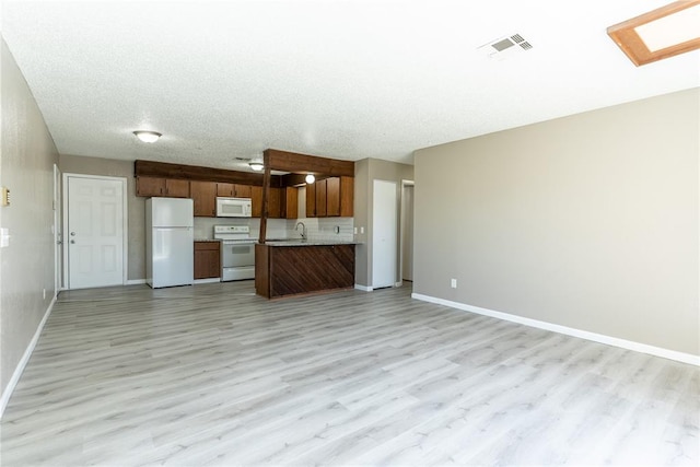 kitchen with a skylight, sink, light hardwood / wood-style floors, a textured ceiling, and white appliances