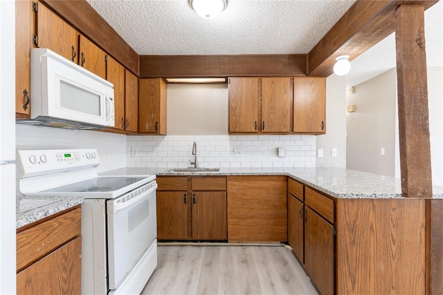 kitchen featuring white appliances, sink, light wood-type flooring, a textured ceiling, and kitchen peninsula