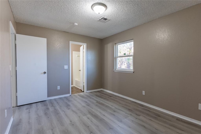 unfurnished bedroom featuring light hardwood / wood-style floors, a textured ceiling, and ensuite bath