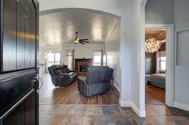 living room with dark hardwood / wood-style flooring, a fireplace, ceiling fan with notable chandelier, and ornamental molding