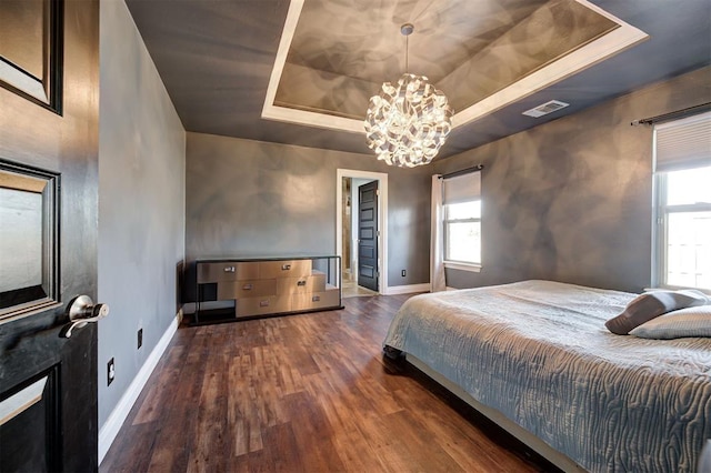 bedroom featuring a tray ceiling, dark wood-type flooring, and an inviting chandelier